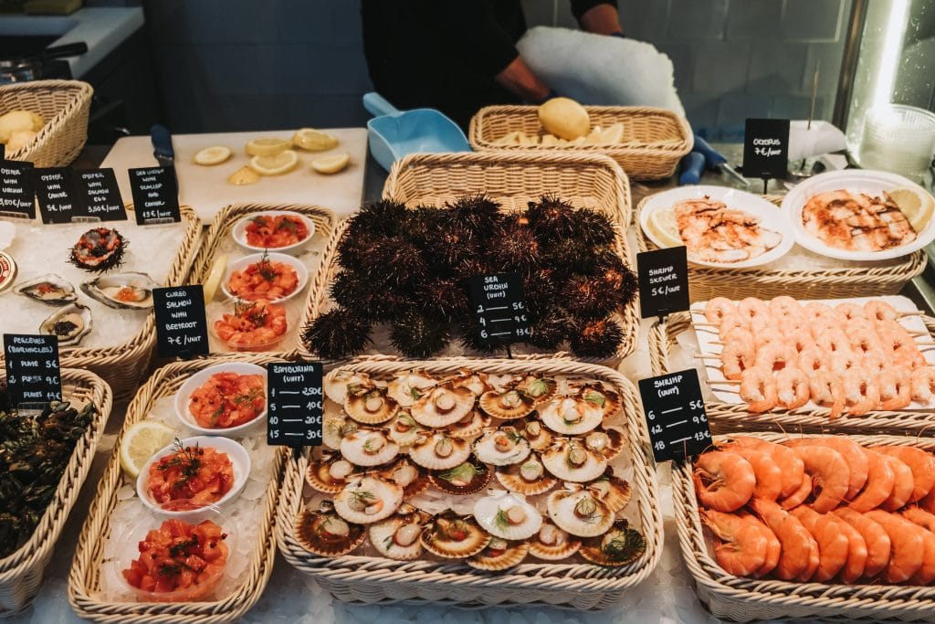 A vibrant display of seafood at Bolhão Market in Porto features scallops, prawns, sea urchins, and clams, each basket meticulously labeled with names and prices.