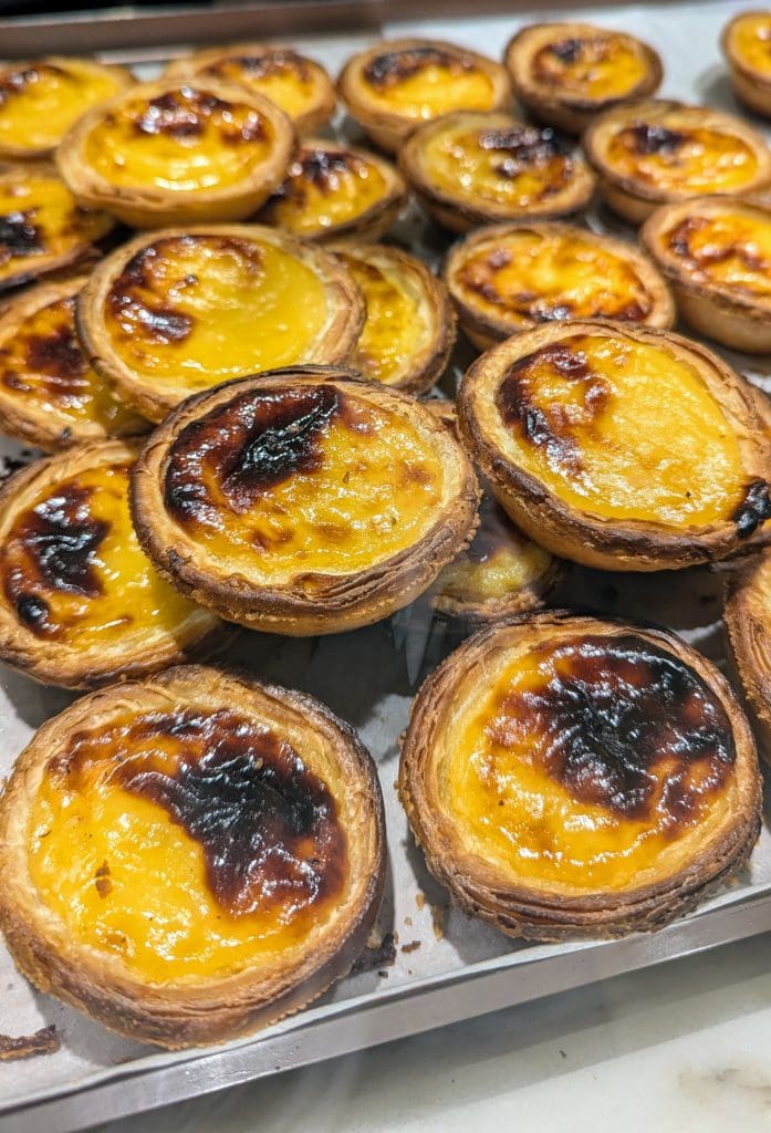 A tray filled with multiple pastel de nata, the classic Portuguese egg tarts, featuring a golden-brown, caramelized top and flaky crusts.