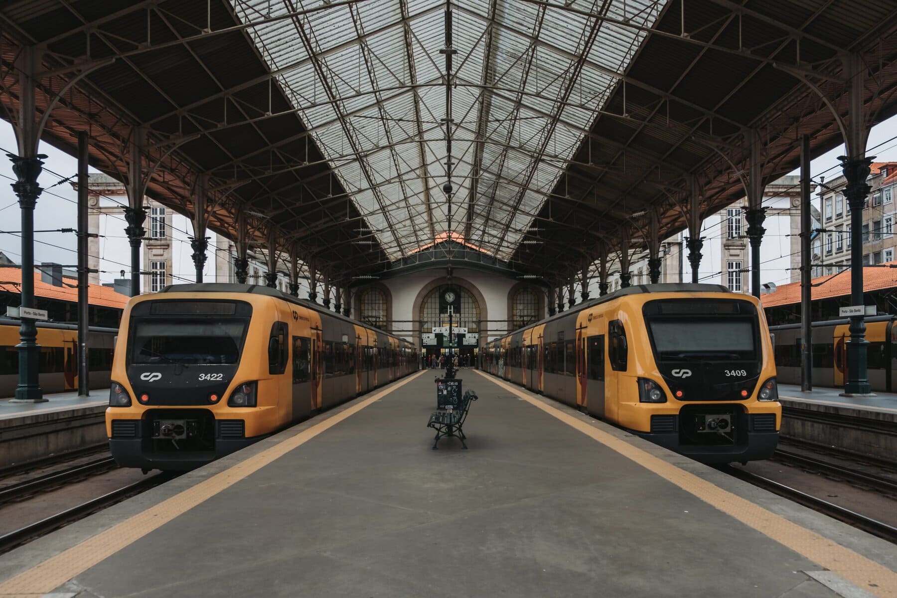 Two yellow and black trains are stationed on parallel tracks in an indoor railway station with a high, arched roof and metal beams.