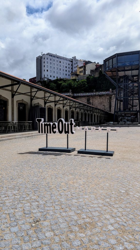 Outdoor view of Porto's "Time Out Market" sign in front of industrial-style buildings, with a cloudy sky in the background.