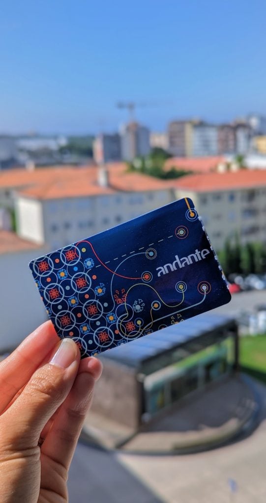 A hand holds an "andante" card against a backdrop of a cityscape with buildings and a partly cloudy sky.