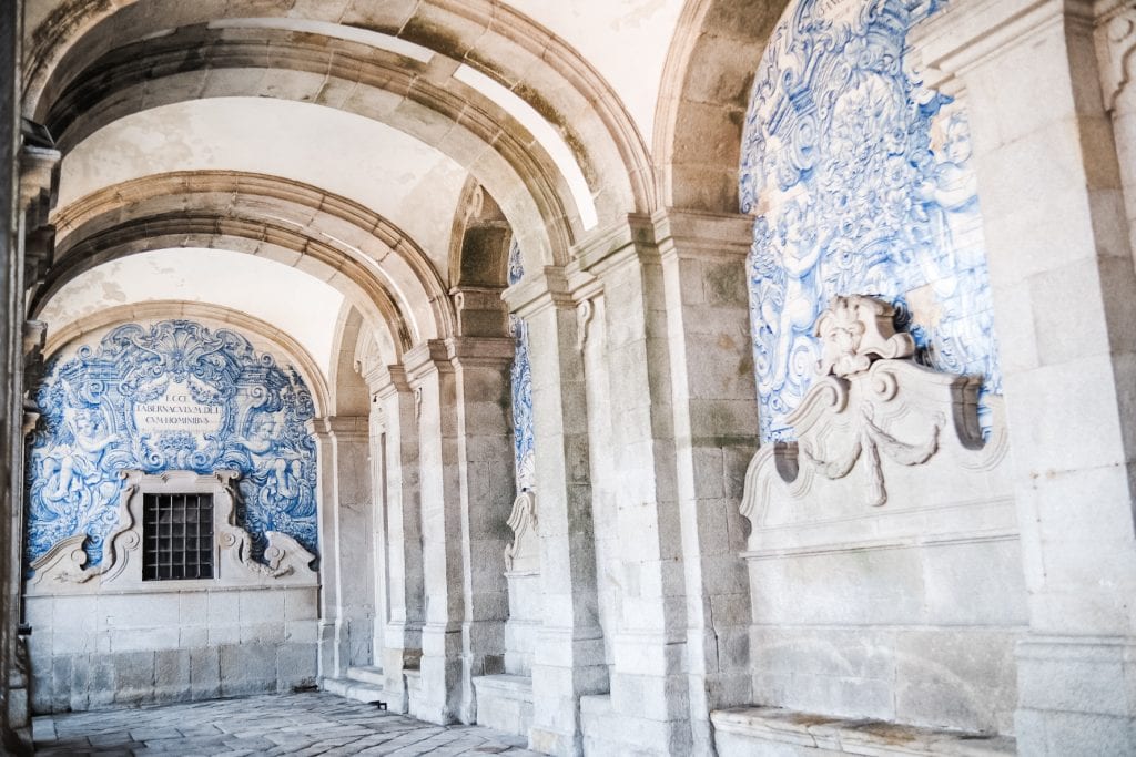 A stone corridor with arched ceilings and intricate blue and white tile murals on the walls.