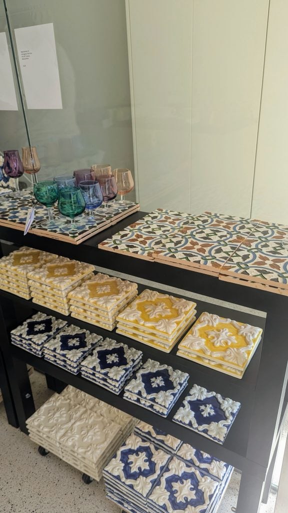 A display shelf with colorful tiles and glassware. The tiles feature intricate patterns and are neatly stacked in various designs, while multiple wine glasses are arranged on the top shelf.