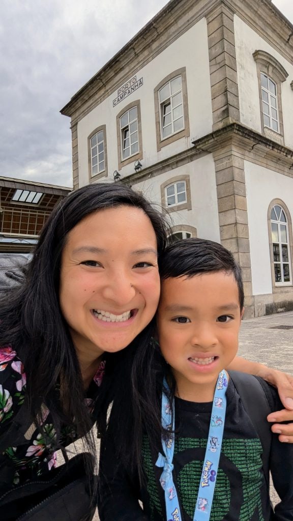 A woman and a young child smile at the camera in front of a building labeled "Porto Campanha." The woman is wearing a floral top, and the child has a blue lanyard with cartoon designs.