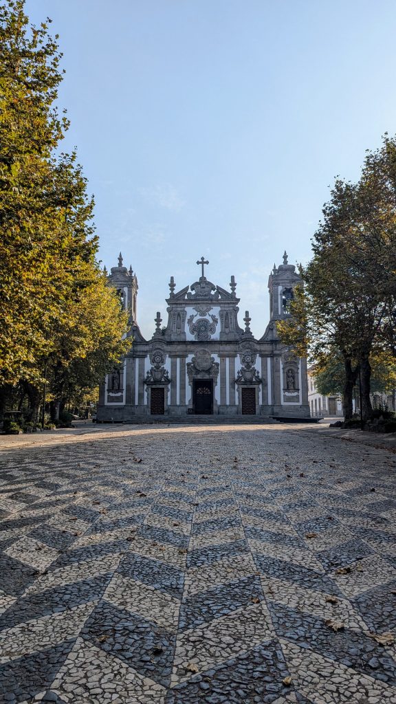 Stone-paved pathway leading to a historic church facade with twin bell towers and intricate architectural details, framed by trees on either side under a clear sky.