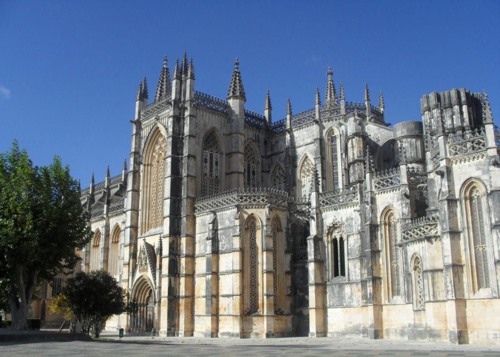 Batalha Monastery in Portugal, featuring Gothic architecture with ornate spires and arched windows, set against a clear blue sky.