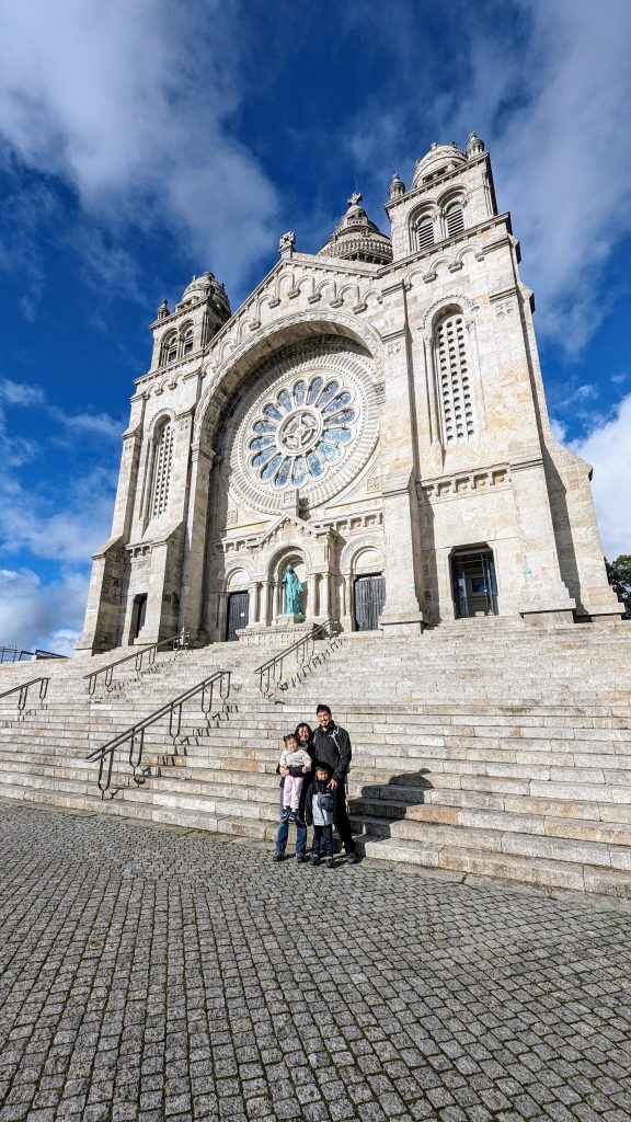 A family stands on the steps of a large stone church featuring intricate architecture and a prominent circular stained glass window.