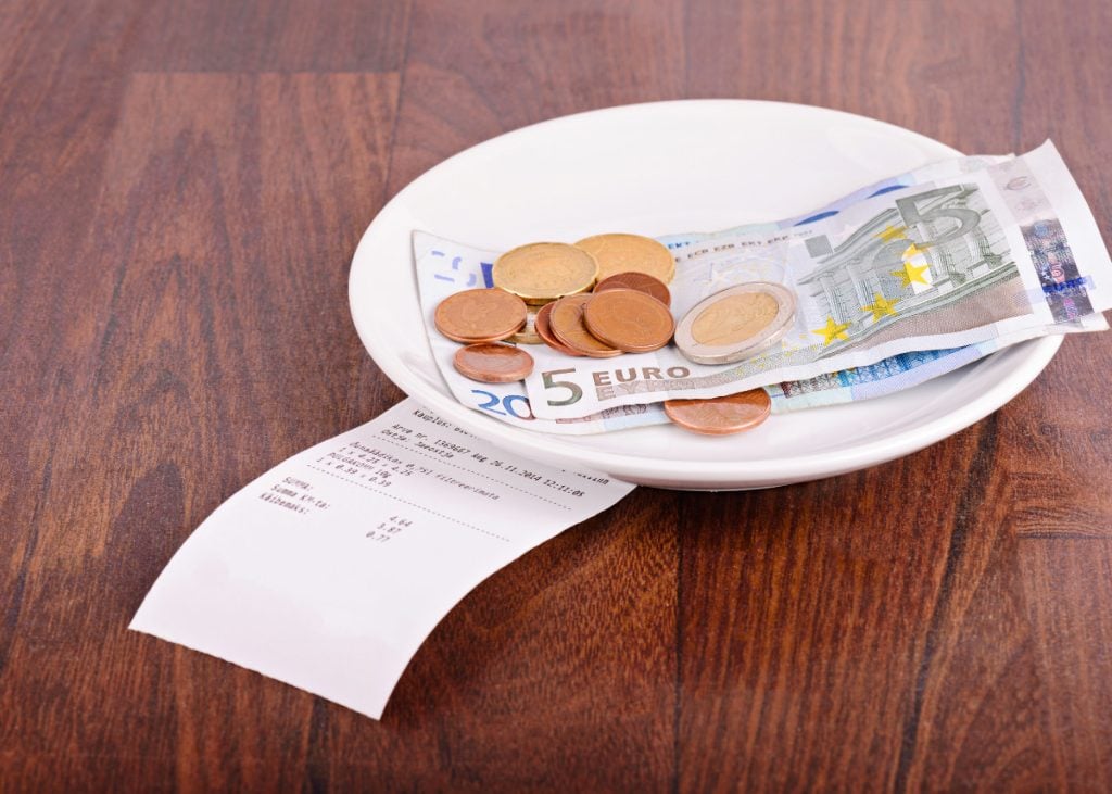A white plate contains euro coins and banknotes, placed on a wooden table with a printed receipt next to it.