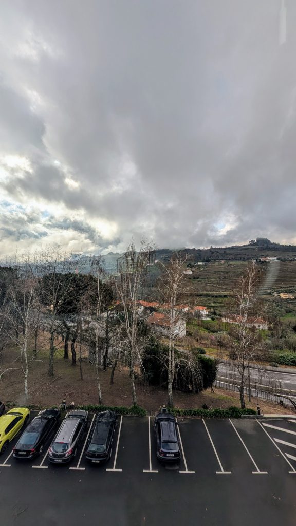 Overcast sky over a rural landscape with parked cars in the foreground and rolling hills in the background.