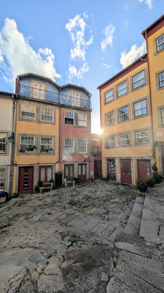 A cobblestone courtyard surrounded by yellow and orange residential buildings under a blue sky with scattered clouds.