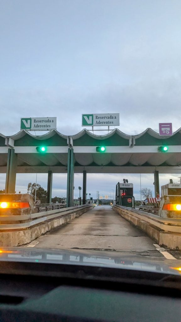 View from a car approaching a Via Verde toll booth with green lights, two lanes marked "Reservada a Adherentes" and one lane for electronic payment.